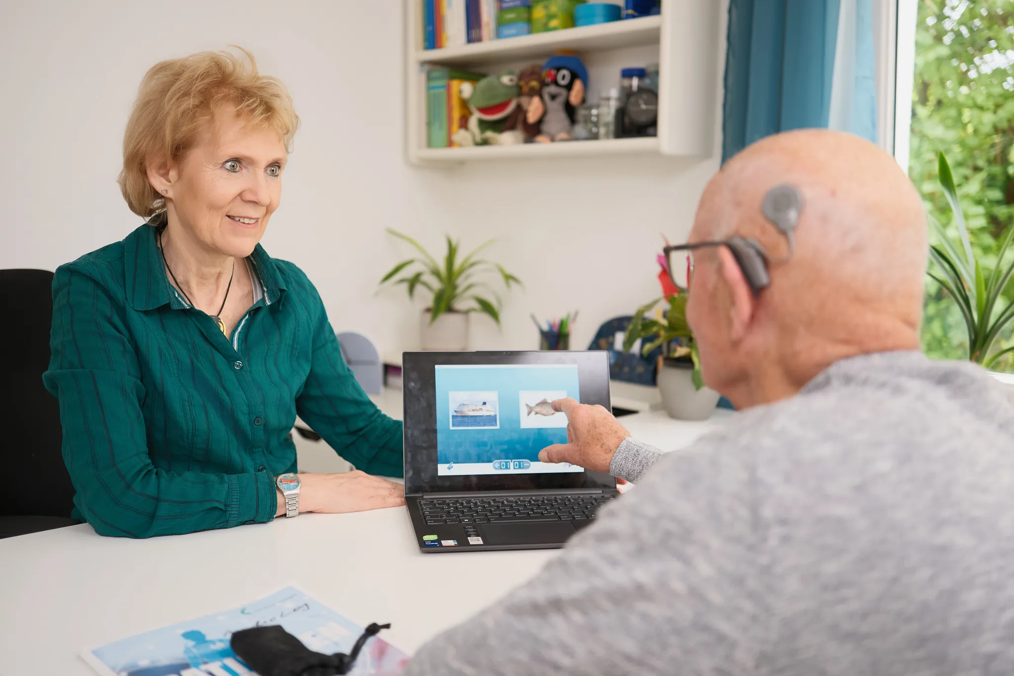 Hörtraining nach Cochlea-Implantation: Therapeutin übt mit einem Patienten am Laptop