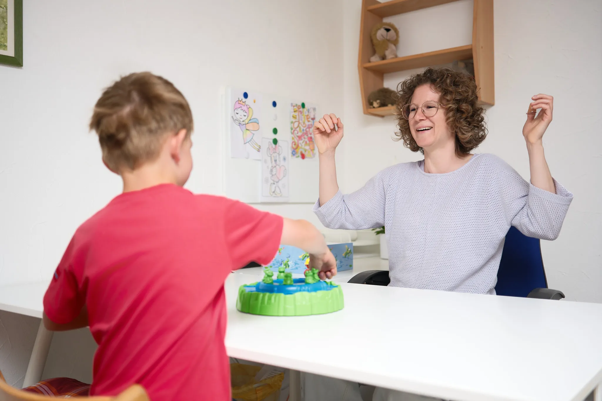 Logopädin lacht mit einem Jungen beim Spiel am Tisch