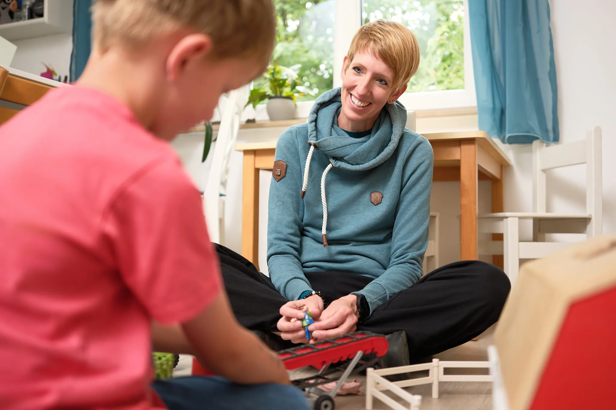 Logopädin sitzt mit einem Jungen beim Spielen auf dem Boden